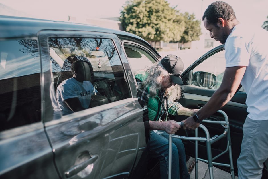 Patient avec un déambulateur aidé à monter dans le véhicule pour un trajet médical